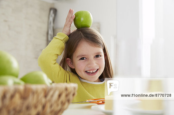 Mädchen am Tisch sitzend mit grünem Apfel