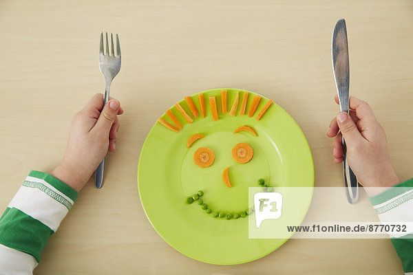 Junge isst Erbsen und Karotten mit anthropomorphem Gesicht.