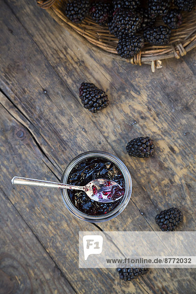 Basket of blackberries (Rubus sectio Rubus) and preserving jar of blackberriy jelly on wooden table