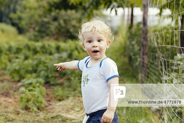 Kleinkind zeigt auf etwas im Gemüsegarten