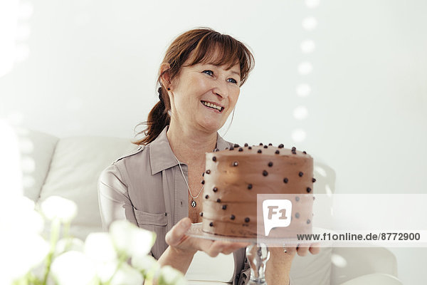Portrait of smiling woman holding cake stand with chocolate cake
