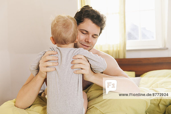 Father sitting in bed  lifting up toddler