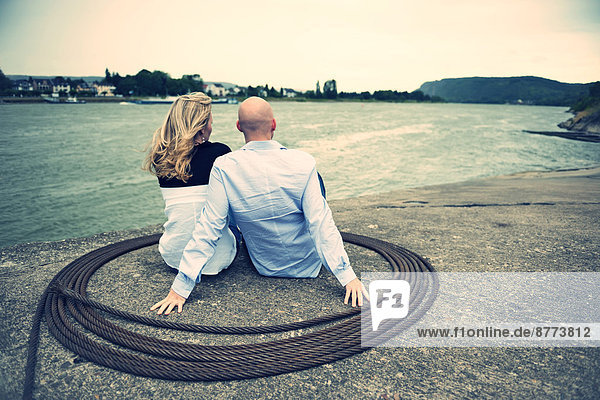 Germany  Rhineland-Palatinate  young couple sitting at waterside of Rhine river