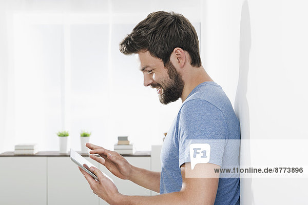 Portrait of young man leaning against wall using mini tablet
