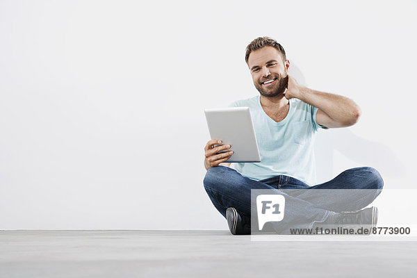 Portrait of young man sitting on floor  using tablet computer