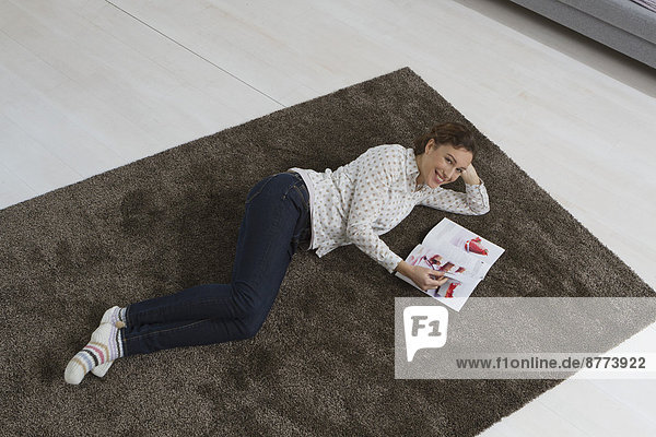 Woman lying on carpet reading magazine