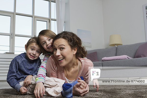 Glückliche Mutter  Sohn und Tochter auf Teppich im Wohnzimmer liegend