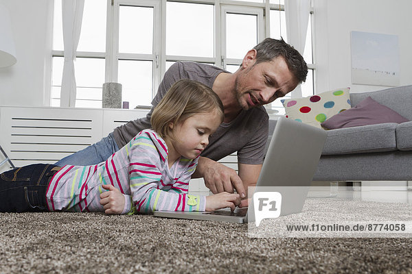 Father and daughter using laptop on carpet in living room