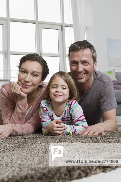 Glückliche Mutter  Vater und Tochter auf Teppich im Wohnzimmer liegend