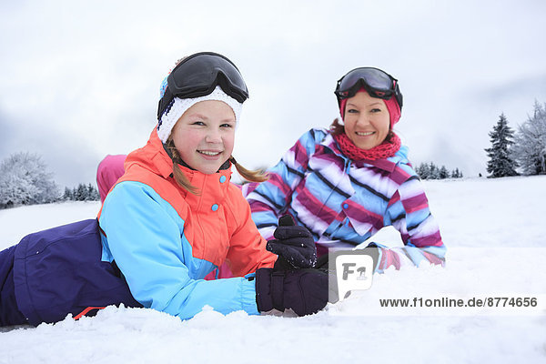 Germany  Masserberg  Mother and daughter lying in snow  smiling happily