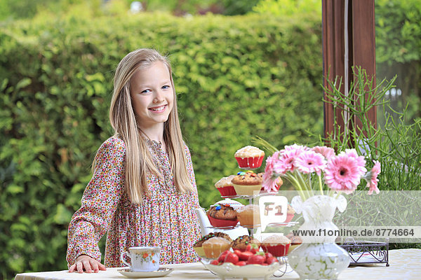 Porträt eines lächelnden Mädchens  das hinter einem gedeckten Tisch steht.
