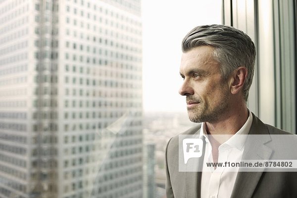 Porträt eines reifen Geschäftsmannes mit Blick aus dem Bürofenster