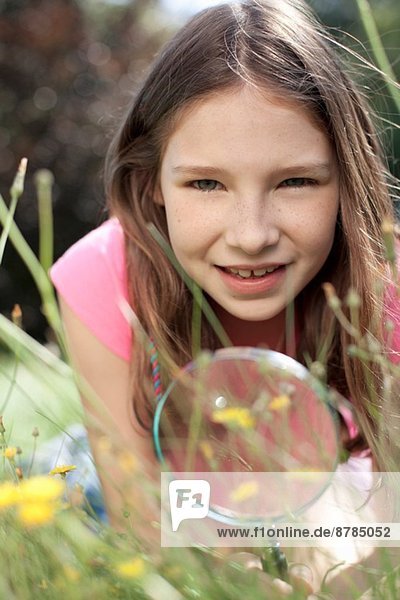 Portrait eines im Gras liegenden Mädchens mit Lupe