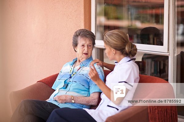 Betreuerin im Gespräch mit Seniorin auf dem Sofa