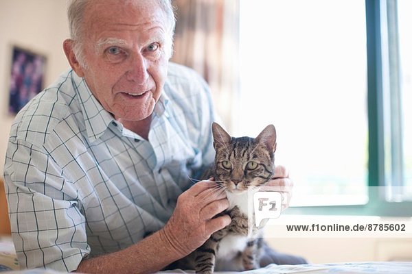Porträt eines älteren Mannes  der eine Hauskatze streichelt.