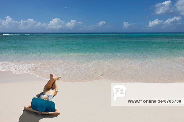 Junge Frau entspannt am Strand mit blauem Sonnenhut