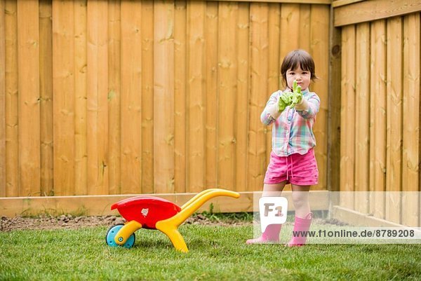Junges Mädchen mit Spielzeug Schubkarre beim Anziehen von Gartenhandschuhen