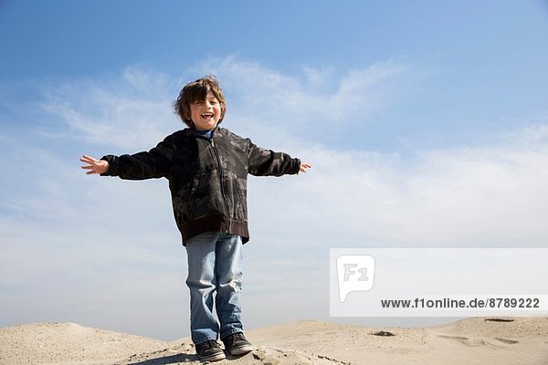 Lächelnder Junge auf Sand stehend mit ausgestreckten Armen
