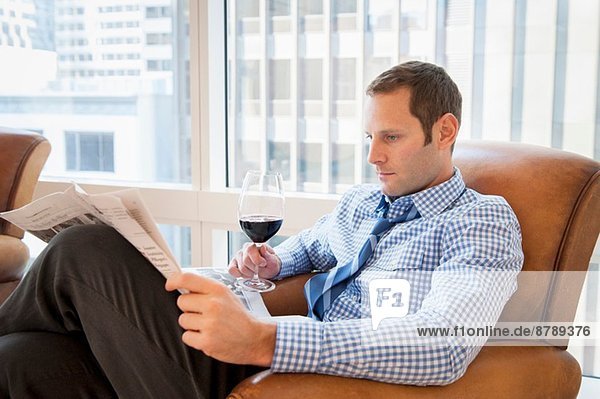 Mittlerer Erwachsener Mann entspannt zu Hause bei Wein und Zeitung