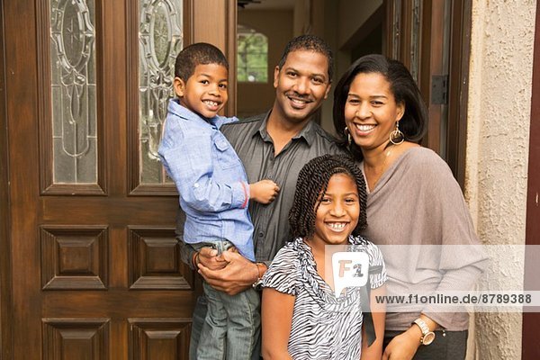 Portrait of mid adult parents with son and daughter at front door
