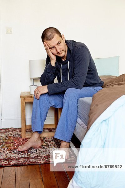 Unglücklicher erwachsener Mann auf dem Bett sitzend mit Kopf in der Hand