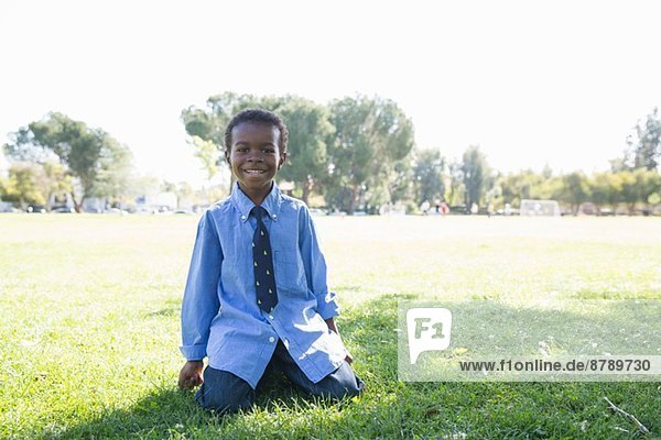 Porträt eines Jungen  der auf Gras kniend in einem sonnigen Park steht