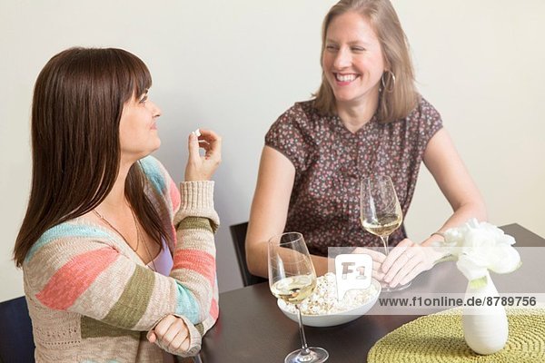 Mittlere erwachsene weibliche Freunde  die Weißwein trinken und Popcorn essen