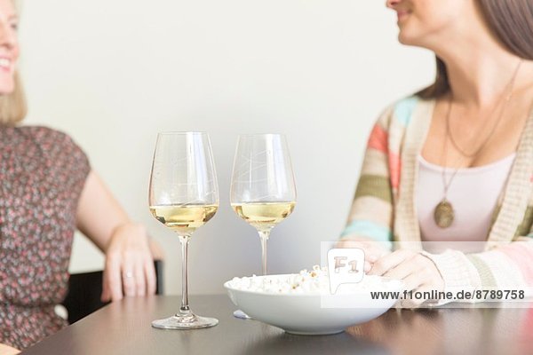 Mittlere erwachsene weibliche Freunde  die bei Tisch mit Wein und Popcorn trinken