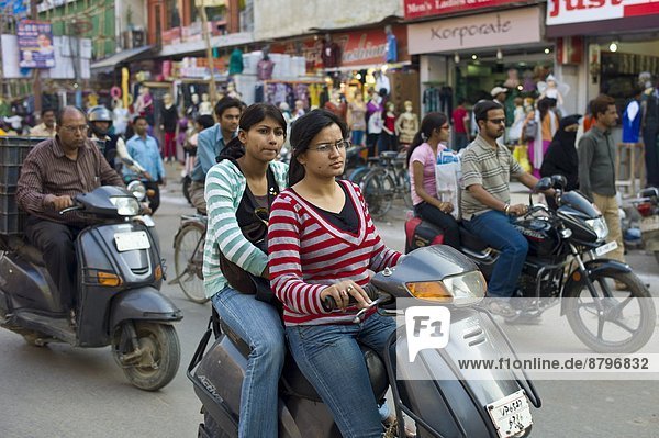 Young Indian girls ride motor scooter in street scene in city of Varanasi  Benares  Northern India