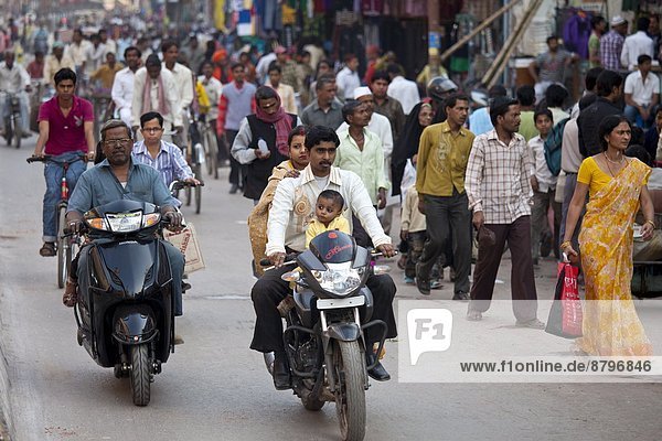 Fathers with children on cycles in crowded street scene during holy Festival of Shivaratri in city of Varanasi  Benares  Northern India