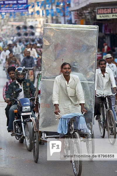 Indian man driving rickshaw with heavy load in street scene in city of Varanasi  Benares  Northern India