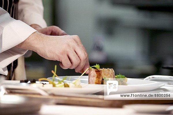 Koch garniert Schweinegericht auf Teller in der Restaurantküche