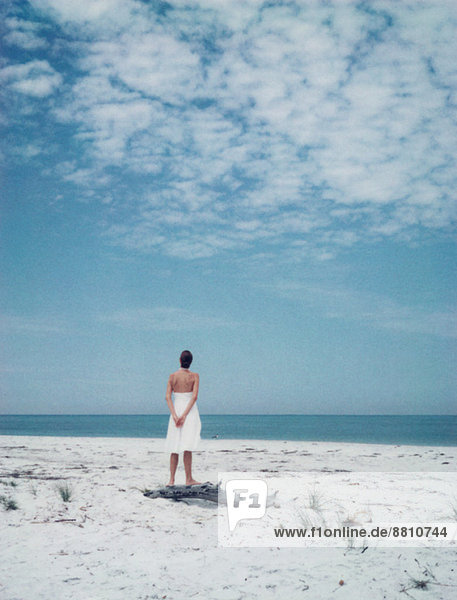 Frau am Strand stehend  Blick zum Horizont  Rückansicht