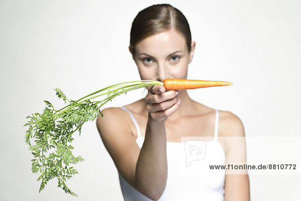 Junge Frau hält rohe Karotte hoch