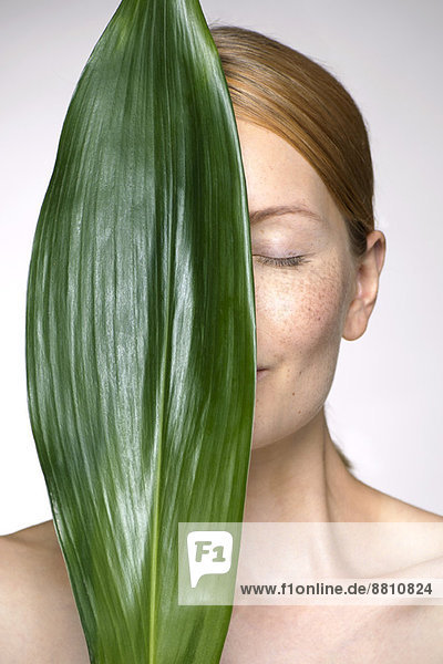 Junge Frau hält Blatt hoch  das einen Teil des Gesichtes verdeckt