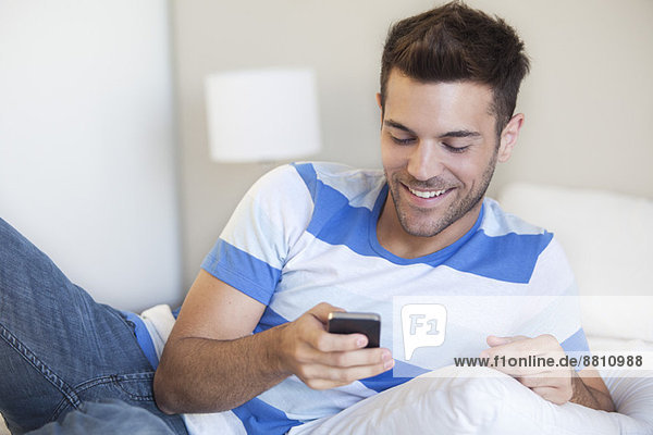 Junger Mann auf dem Bett liegend mit Blick auf das Smartphone