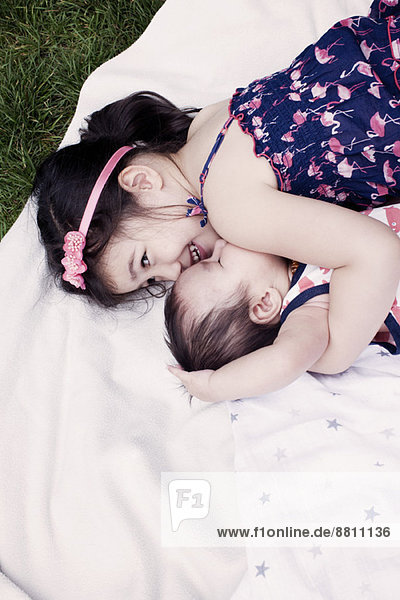 Kleines Mädchen mit Baby-Bruder auf der Decke im Freien liegend