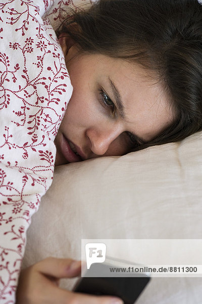 Frau liegt Bett Blick auf Smartphone mit unglücklichem Ausdruck im Gesicht