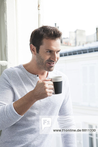 Man looking out of window with mug in hand