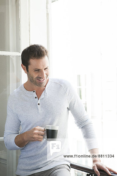 Man standing by window with mug in hand