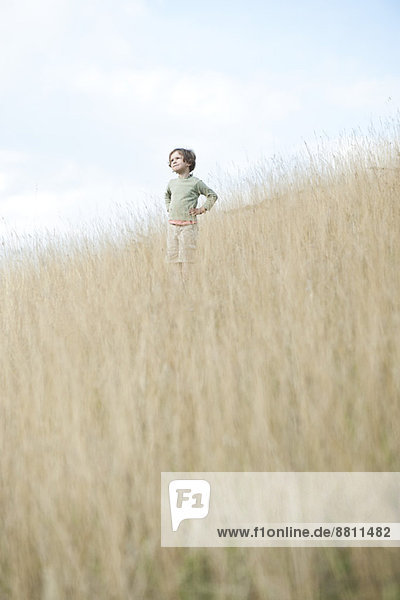 Boy standing in tall grass  looking away in thought