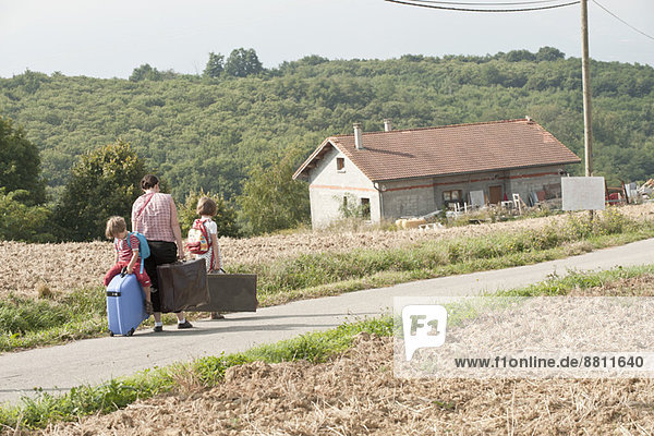 Mutter und Kinder wandern durch die Landschaft und ziehen Koffer hinter sich her.