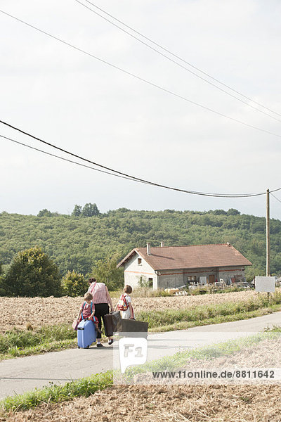 Mutter und Kinder wandern durch die Landschaft und ziehen Koffer hinter sich her.