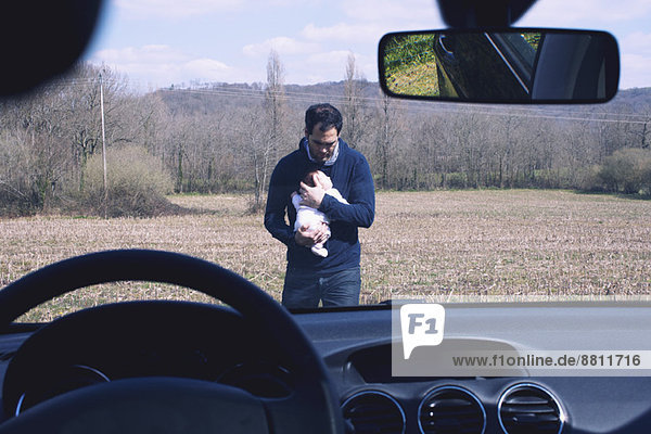 Father holding baby  seen through car windshield