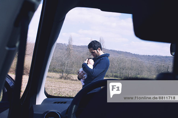 Vater hält Baby  durch die Windschutzscheibe des Autos gesehen