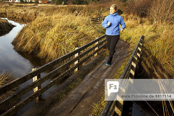 Europäer Frau über Brücke Holz Bach joggen