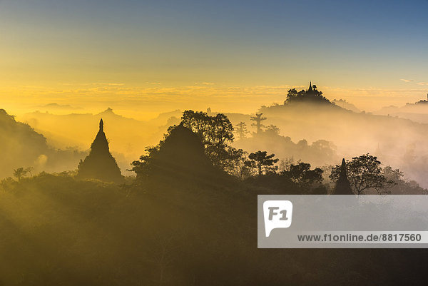 Pagodas surrounded by trees in the mist in the morning light Mrauk U Sittwe District Rakhine State Myanmar