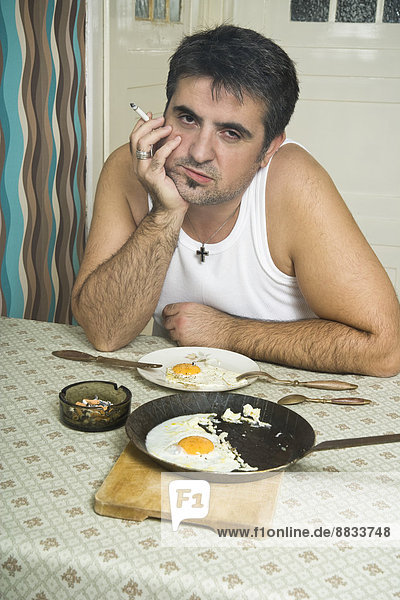 Porträt eines Mannes mit schlechter Angewohnheit  der am Frühstückstisch sitzt.