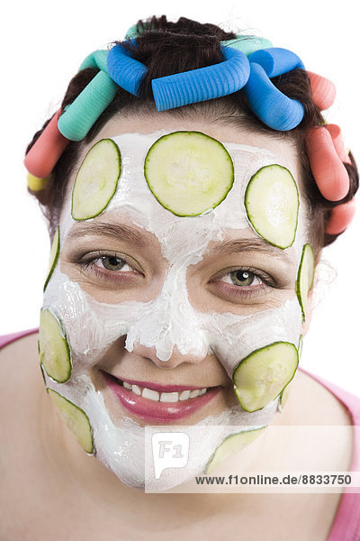Porträt der lächelnden Frau mit Lockenwickler und Schönheitsmaske mit Gurkenscheiben