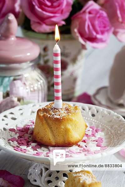 Muffin mit angezündeter Geburtstagskerze  Glas Marshmallows  Tasse und rosa Rosen auf Tisch